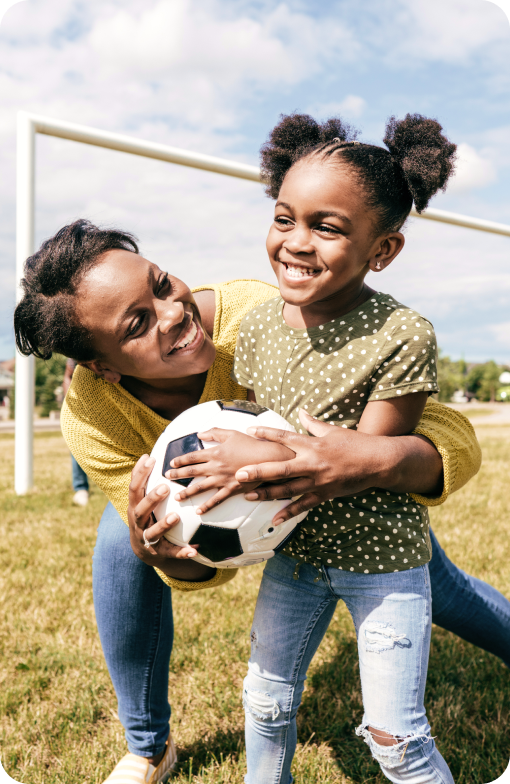 Madre que juega al aire libre junto a su hija con una pelota de fútbol.